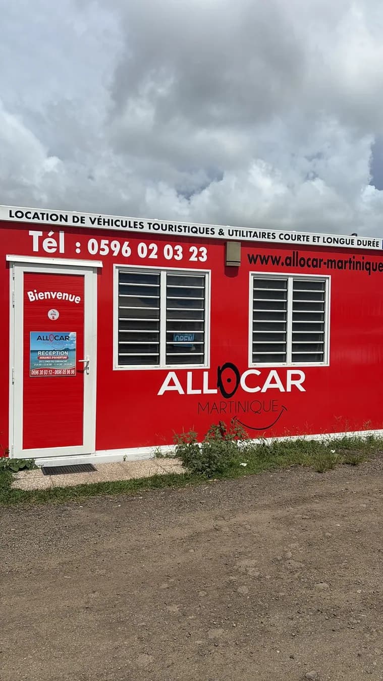 Façade rouge d'une agence de location avec deux fenêtres et des inscriptions blanches